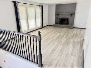 Unfurnished living room with light wood finished floors, a brick fireplace, and a textured ceiling