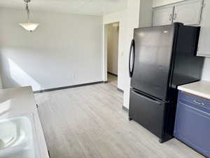 Kitchen with light countertops, light wood-style floors, freestanding refrigerator, blue cabinetry, and a textured ceiling