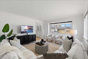 Front living room with decorative paneled wainscot, large windows, carpet flooring and light paint
