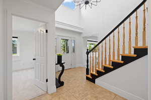 Foyer featuring a chandelier, two-tone stair railing, light colored paint, two-story ceilings and tile flooring