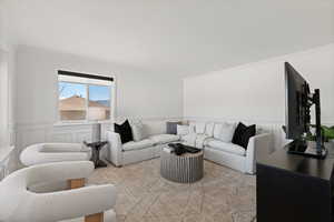 Front living room with decorative paneled wainscot, large windows, carpet flooring and light paint