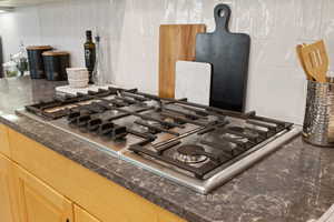 Detail view of 5-burner gas cooktop, quartz counter tops, and tile backsplash