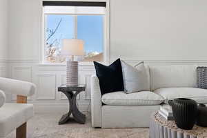 Front living room with decorative paneled wainscot, large windows, carpet flooring and light paint