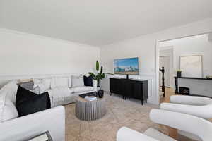 Front living room with decorative paneled wainscot, large windows, carpet flooring and light paint
