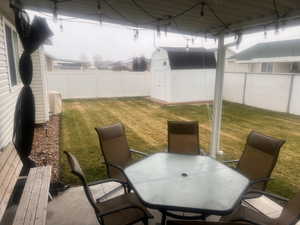Fenced backyard with outdoor dining space, a storage unit, and a sunroom