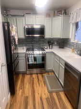 Kitchen with stainless steel appliances, decorative backsplash, light wood-style flooring, and light stone counters