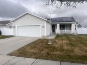 Ranch-style home featuring a gate, roof mounted solar panels, covered porch, a garage, and driveway