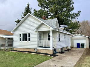 View of front of home featuring an outbuilding, a garage, driveway, a shingled roof, and covered porch