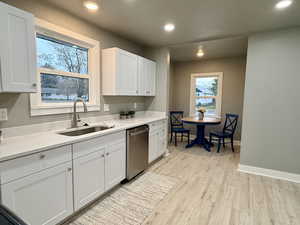 Kitchen featuring white cabinetry, stainless steel dishwasher, light wood-style flooring, recessed lighting, and light stone counters