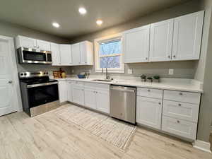 Kitchen featuring stainless steel appliances, white cabinets, light wood-style floors, recessed lighting, and light stone countertops