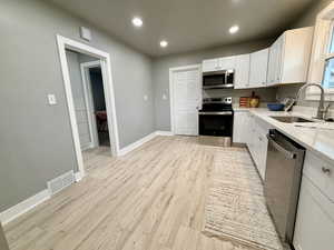 Kitchen with stainless steel appliances, white cabinets, light stone countertops, recessed lighting, and light wood-style floors