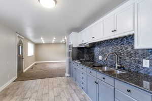Kitchen featuring wood finish floors, dark stone counters, white cabinets, stainless steel appliances, and backsplash
