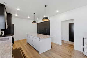 Kitchen featuring light stone counters, a center island, light wood finished floors, a breakfast bar area, and pendant lighting