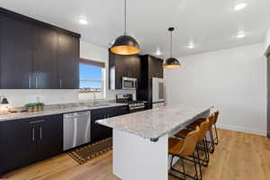 Kitchen featuring stainless steel appliances, a center island, light wood-style floors, light stone counters, and pendant lighting