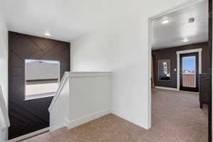 Hall with an upstairs landing, light carpet, and a textured ceiling
