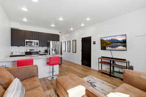 Kitchen featuring light stone countertops, a breakfast bar, stainless steel appliances, light wood-type flooring, and dark wood finish cabinetry