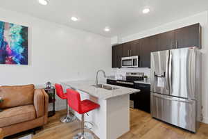 Kitchen with stainless steel appliances, a peninsula, a kitchen bar, light stone countertops, and light wood-type flooring