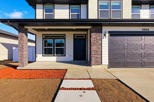 Entrance to property with a porch, stone siding, concrete driveway, and an attached garage
