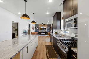Kitchen featuring stainless steel appliances, light stone countertops, open floor plan, light wood-type flooring, and hanging light fixtures