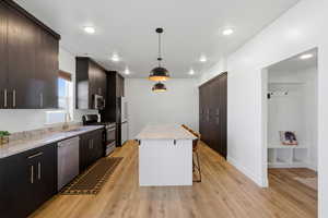 Kitchen with dark wood finish cabinetry, light stone counters, stainless steel appliances, hanging light fixtures, and a breakfast bar