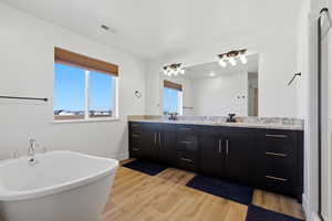 Full bathroom featuring double vanity, light wood-type flooring, and a freestanding bath