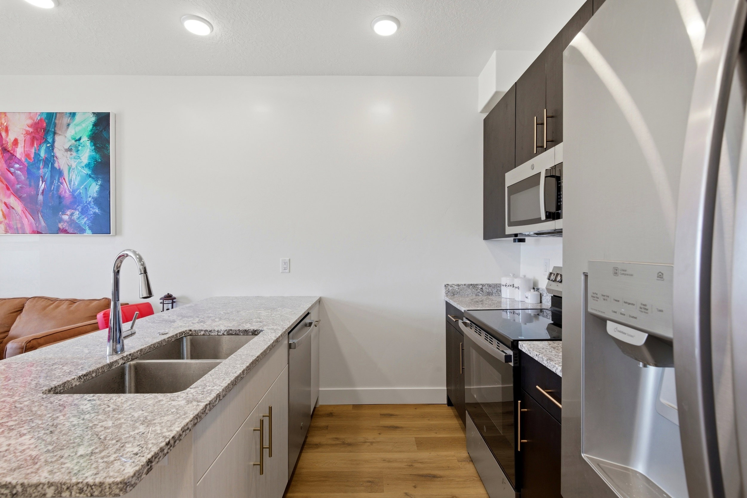 Kitchen featuring stainless steel appliances, a peninsula, light wood-style floors, light stone counters, and dark wood finish cabinets