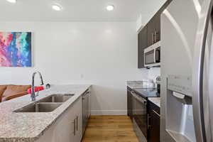 Kitchen featuring stainless steel appliances, a peninsula, light wood-style floors, light stone counters, and dark wood finish cabinets