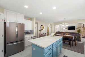 Dual tone kitchen featuring freestanding refrigerator, a center island, open floor plan, arched walkways, and decorative backsplash