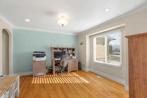 Home office featuring light wood finished floors, arched walkways, ornamental molding, and recessed lighting