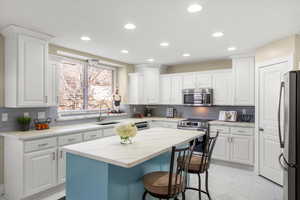 Kitchen with white cabinetry, a breakfast bar, stainless steel appliances, light marble finish floors, and a kitchen island