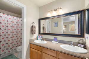 Full bathroom with double vanity, shower / tub combo with curtain, and light tile patterned floors