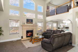 Living room featuring arched walkways, a warm lit fireplace, carpet flooring, and a high ceiling