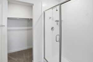 Full bath featuring a spacious closet, a shower stall, and carpet floors