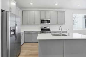 Kitchen featuring stainless steel appliances, gray cabinets, light wood finished floors, a kitchen island with sink, and recessed lighting