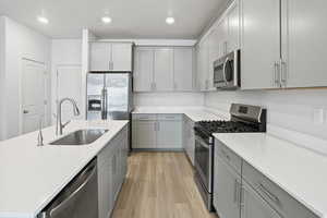 Kitchen featuring stainless steel appliances, gray cabinetry, light wood-type flooring, recessed lighting, and a center island with sink