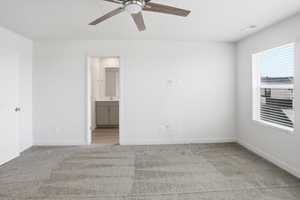 Unfurnished bedroom featuring light carpet, ensuite bath, and a ceiling fan