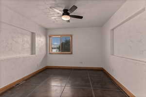Empty third bedroom with a textured wall, a ceiling fan, and dark tile patterned flooring