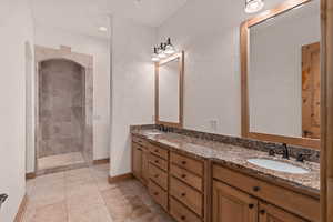Bathroom with double vanity, a tile shower, a textured wall, light tile patterned floors, and recessed lighting