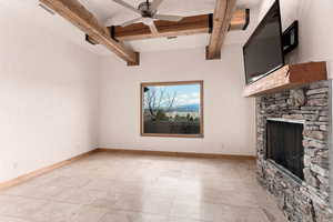 Unfurnished living room featuring a ceiling fan, beam ceiling, and a stone fireplace