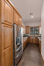 Butler's Kitchen featuring concrete flooring, stainless steel fridge, dark stone countertops, and recessed lighting