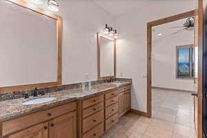 Full bath featuring double vanity, a ceiling fan, light tile patterned flooring, a textured wall, and vaulted ceiling