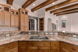 Kitchen with light stone countertops, beamed ceiling, recessed lighting, glass fronted cabinets, and built in features