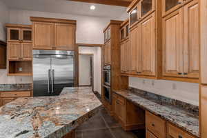 Kitchen featuring glass insert cabinets, stainless steel appliances, light stone counters, recessed lighting, and built in desk