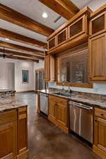 Kitchen with concrete flooring, dark stone counters, beamed ceiling, wood finish cabinetry, and dishwasher