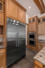 Kitchen with finished concrete floors, stainless steel appliances, dark stone counters, glass insert cabinets, and recessed lighting