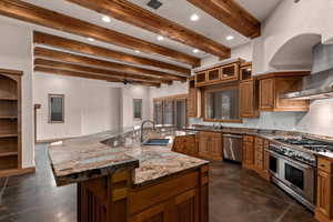 Kitchen featuring beam ceiling, light stone countertops, stainless steel appliances, wood finish cabinetry, and concrete floors