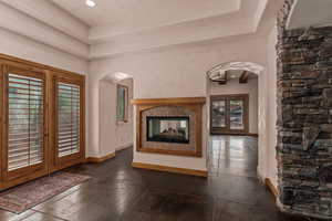Unfurnished dining room with french doors, arched walkways, a raised ceiling, and a multi sided fireplace