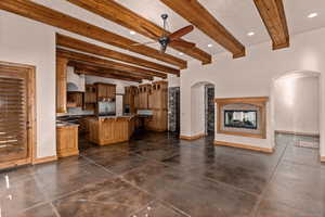 Kitchen featuring beamed ceiling, a kitchen island with sink, ceiling fan, glass insert cabinets, and a multi sided fireplace