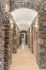 Hallway featuring a barrel ceiling, arched walkways, and light tile patterned flooring