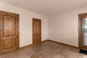 Empty bedroom with door on left leading to hallway/entrance of home, door in middle leading to bathroom, and door on right that leads to outside (west side of house)